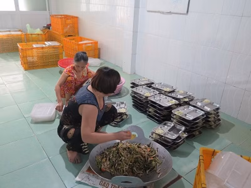 Nhân viên không có bảo hộ lao động đang múc thức ăn ra khay chuẩn bị giao hàng