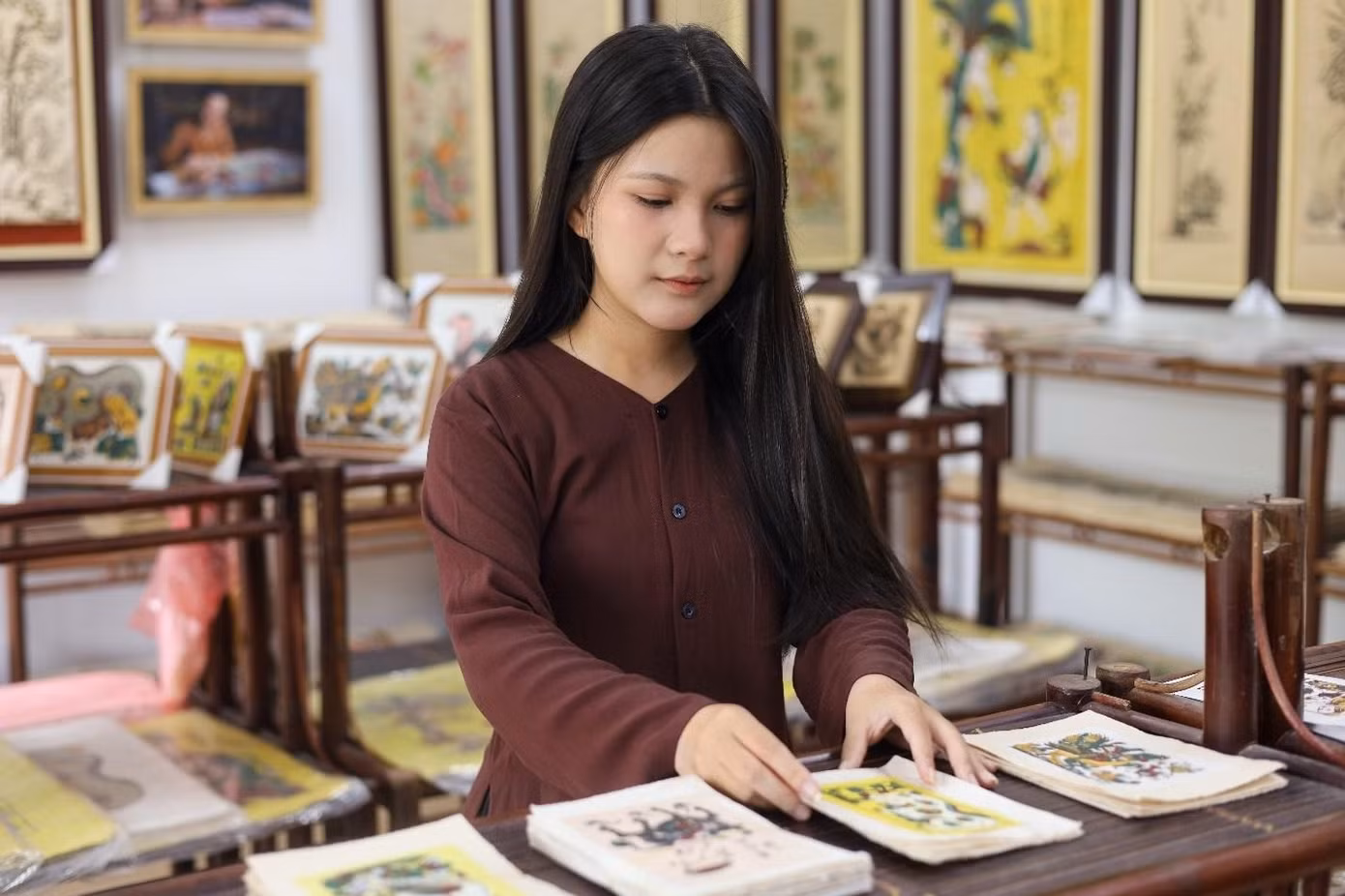 Không chỉ trực tiếp lắng nghe những lời chỉ dạy về nghề, Nguyễn Thảo My còn là trợ thủ đắc lực giúp ông nội sắp xếp và kiểm tra từng bức tranh sau khi in xong, như một cách để cô thẩm thấu trọn vẹn giá trị của di sản gia đình. Đây là sự giao thoa giữa hai thế hệ khi Nguyễn Thảo My trực tiếp tiếp thu những giá trị truyền thống từ ông nội để chuẩn bị cho hành trình đưa tranh Đông Hồ đến gần hơn với giới trẻ. (Ảnh: Minh Hiền)