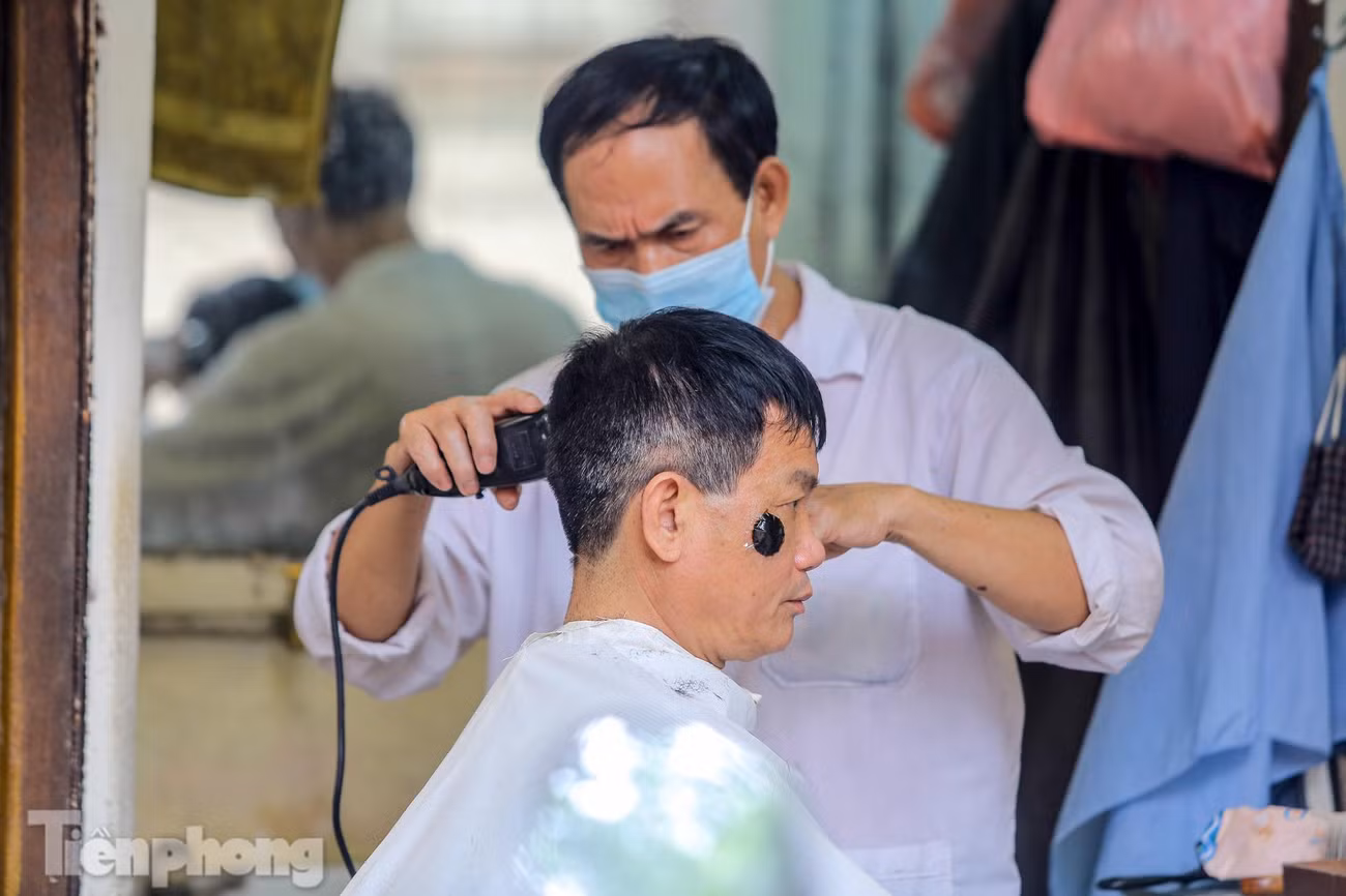 Một thợ cắt tóc ở phố Tràng Thi tranh thủ cắt cho khách quen trước giờ đóng cửa.