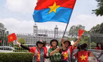 Người dân vẫy cờ Mặt trận Dân tộc Giải phóng miền Nam khi chụp ảnh trước Dinh Độc Lập ngày 29/4. (Ảnh: AP)