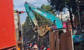 Gầu máy xúc đầy đất lơ lửng trên đầu người đi đường