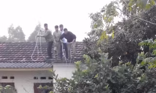 Người dân phải đứng trên nóc nhà, quăng dây xuống nhằm giăng bẫy bắt "trâu điên". Ảnh cắt từ clip do nhân chứng cung cấp.