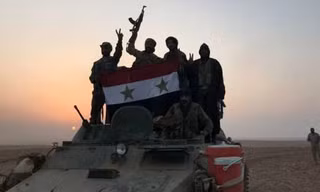 Quân đội Syria cầm quốc kì ăn mừng sau khi tiến vào thị trấn Albu Kamal hồi đầu tháng 11. Ảnh: AFP