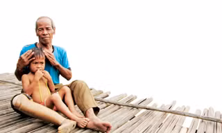 Ông Mơ đang ôm cháu Hồ Dừa (4 tuổi, mồ côi cha mẹ) vào lòng nâng niu, vỗ về. Ảnh: H.T.