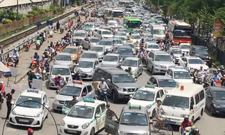 Đường Giải Phóng trước BV Bạch Mai ùn tắc nhưng taxi vẫn dàn hàng đứng đón, trả khách, còn công an có mặt (khoanh tròn) lấy báo che đầu Ảnh: A.Trọng