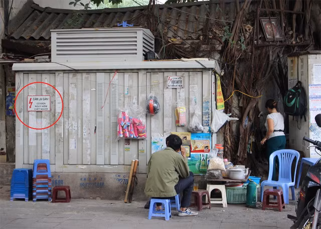 Mặc dù có biển cảnh báo nguy hiểm, không được lại gần ( ở vòng tròn đỏ) tại bốt điện này, nhưng người bán hàng nước và vị khách này vẫn ngồi sát. Ảnh chụp tại vỉa hè phố Vũ Tông Phan