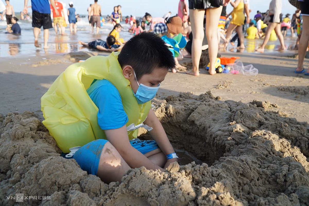 Nguyễn Nhật Thanh, 7 tuổi, đào hố cát. Suốt buổi chiều hôm nay, cậu bé không cởi khẩu trang. "Mẹ con và cô giáo bảo phải đeo để vừa bảo vệ cho mình, cho mọi người tránh Covid -19", bé trai nói.