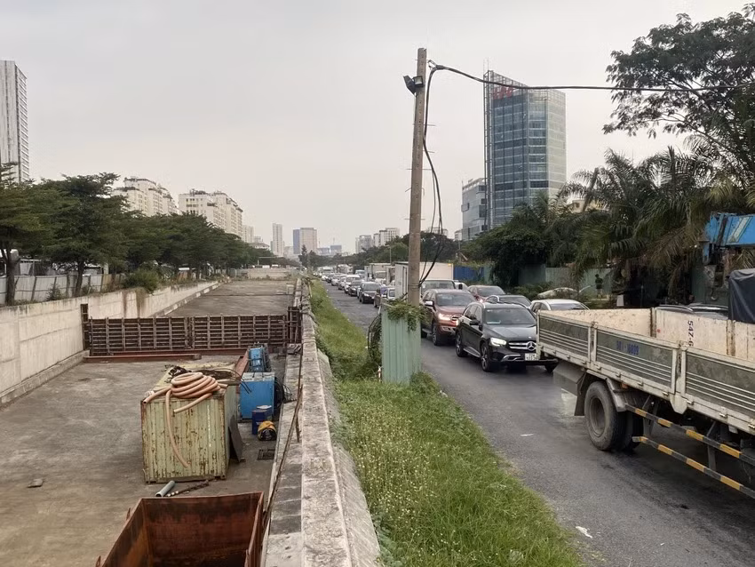 Phía bên trái là công trường, phía phải là cảnh xe tải, ô tô, container xếp hàng dài di chuyển qua khu vực này. Phía bên trái là công trường, phía phải là cảnh xe tải, ô tô, container xếp hàng dài di chuyển qua khu vực này.