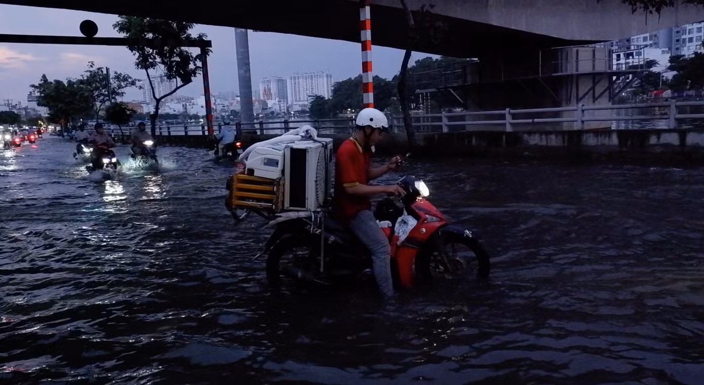 Xe bị "chết máy", một nhân viên cửa hàng điện máy phải loay hoay giữa dòng nước.