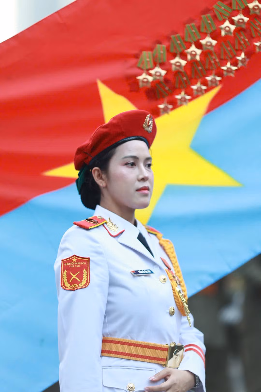 Các nữ chiến sĩ thuộc khối Quân nhạc đứng trang nghiêm trước lá cờ Mặt trận Dân tộc giải phóng miền Nam Việt Nam. Đây là một trong những nữ chiến sĩ đại diện hình ảnh “bông hồng thép” thuộc lực lượng Quân đội Nhân dân Việt Nam.
