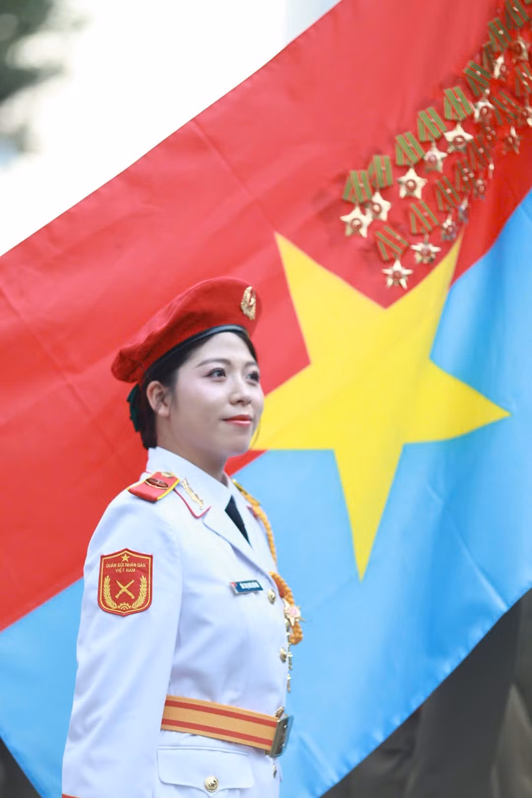 Các nữ chiến sĩ thuộc khối Quân nhạc đứng trang nghiêm trước lá cờ Mặt trận Dân tộc giải phóng miền Nam Việt Nam. Đây là một trong những nữ chiến sĩ đại diện hình ảnh “bông hồng thép” thuộc lực lượng Quân đội Nhân dân Việt Nam.