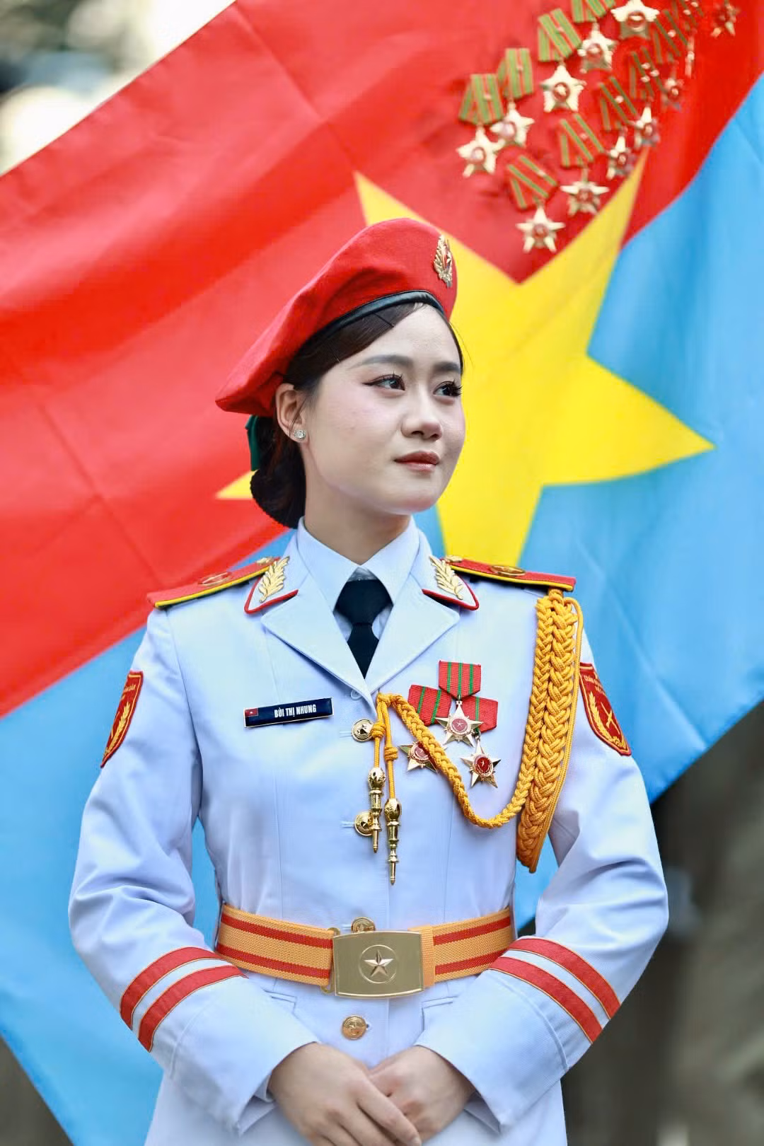 Các nữ chiến sĩ thuộc khối Quân nhạc đứng trang nghiêm trước lá cờ Mặt trận Dân tộc giải phóng miền Nam Việt Nam. Đây là một trong những nữ chiến sĩ đại diện hình ảnh “bông hồng thép” thuộc lực lượng Quân đội Nhân dân Việt Nam.