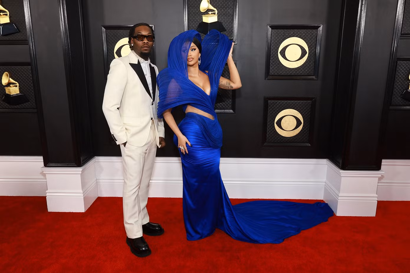 Cardi B dịu dàng khi dự thảm đỏ cùng chồng. Cô giữ lại chút phong cách quái dị với chi tiết vai phồng cao hơn đầu. Chi tiết khoét eo và xẻ ngực tôn lên vẻ gợi cảm cho nữ ca sĩ.