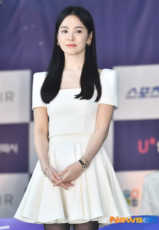 Tại sự kiện in dấu tay, Song Hye Kyo diện váy trên gối, phối cùng tất lưới. Nữ diễn viên trông trẻ trung khi lựa chọn trang phục kiểu dáng cơ bản, đơn sắc. Cách làm tóc và trang điểm cũng giúp nữ diễn viên trông trẻ hơn tuổi thật.