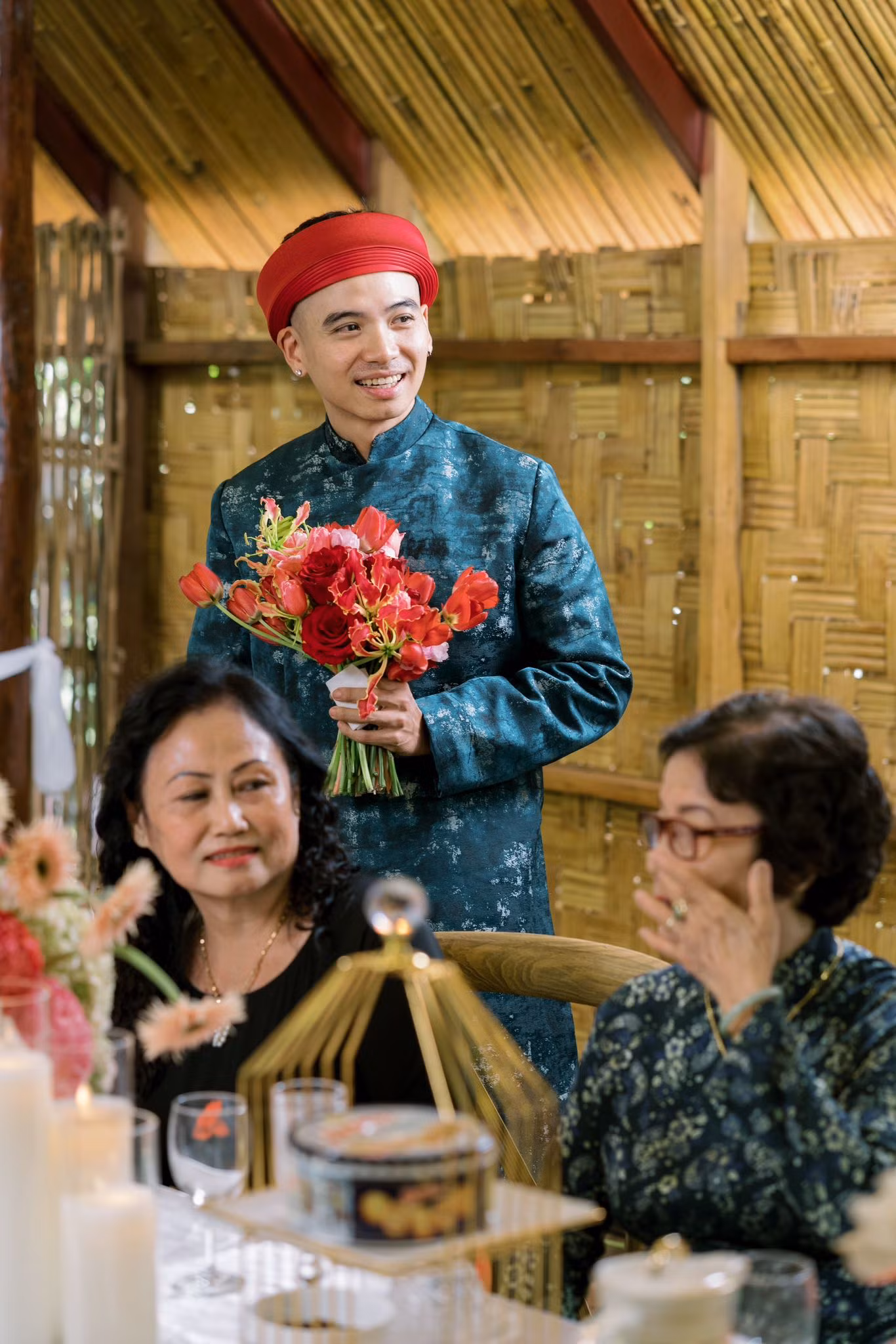 Chú rể Tuấn Khôi mặc áo dài khăn đóng, chào họ nhà gái. Nhiếp ảnh gia cầm bó hoa cưới được kết từ hoa hồng đỏ.