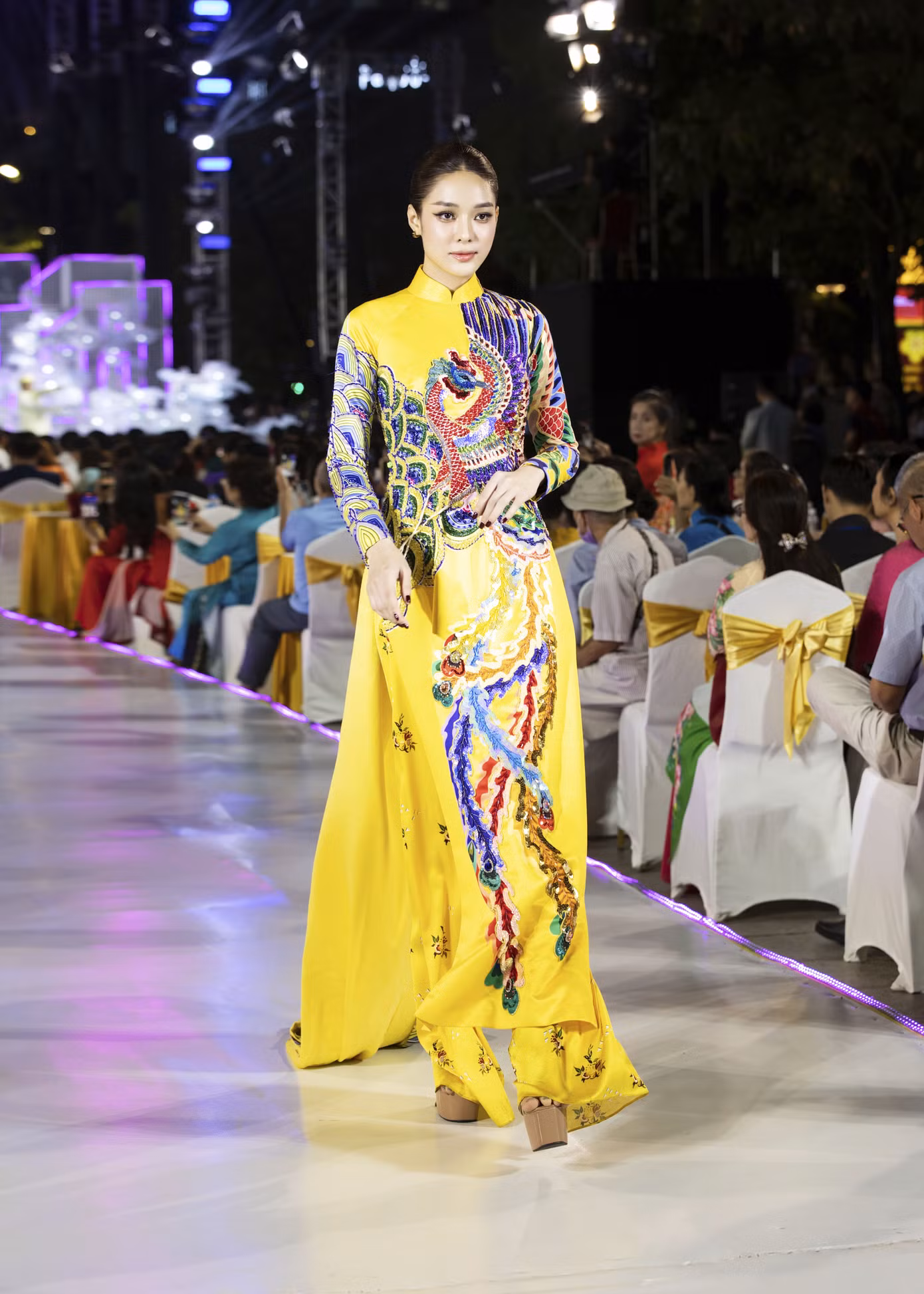 Á hậu Hồng Hạnh diện áo dài vàng in hình chim phượng hoàng ngũ sắc. Thiết kế là trang phục dân tộc của đại diện Việt Nam tại cuộc thi World Miss University 2019.