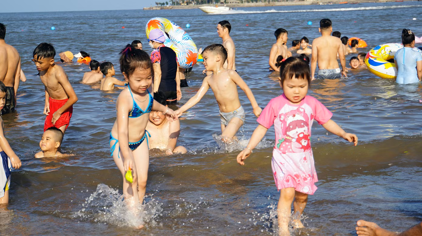 Các em nhỏ nô đùa bên bờ cát, ôm phao tắm biển.