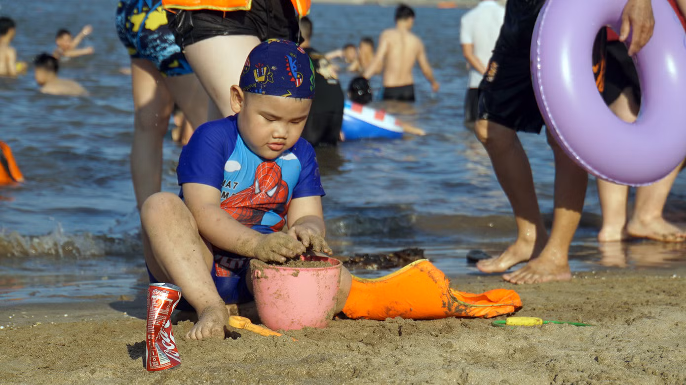 Các em nhỏ nô đùa bên bờ cát, ôm phao tắm biển.