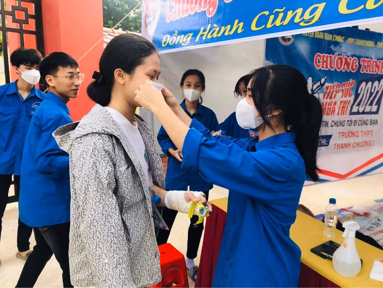 Một thí sinh bị thương ở tay được tình nguyện viên phát và đeo khẩu trang trước khi vào phòng thi