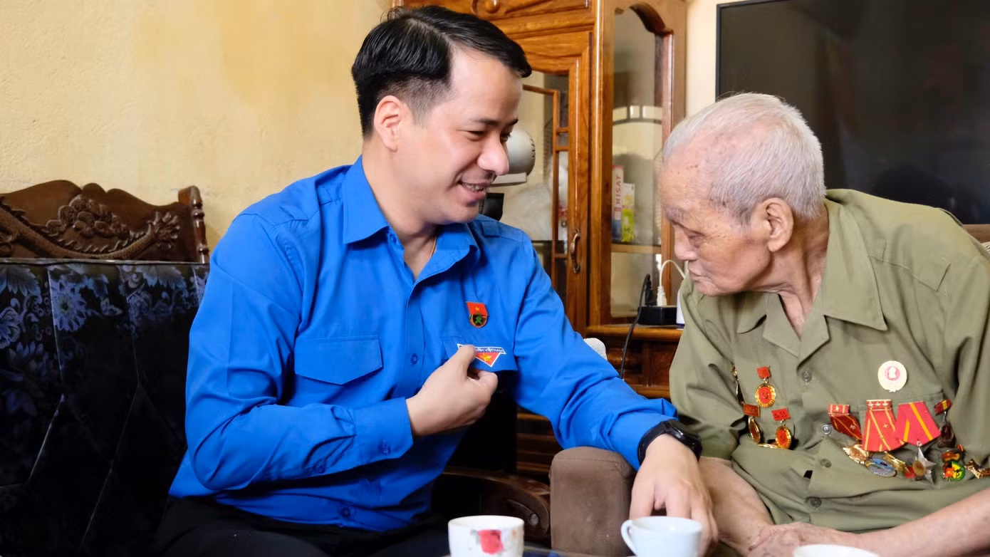 Dù mắt đã kém, ông Hoàng Đình Huệ vẫn chú tâm để đọc được chữ "Thanh niên Việt Nam" trên áo của anh Ngô Văn Cương. Ảnh: Châu Linh