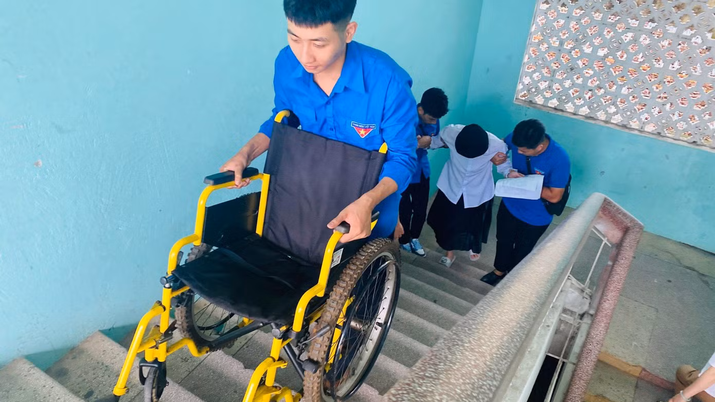 Để kịp giờ thi, các bạn tình nguyện viên đã thay nhau bê cả xe lăn lên cầu thang vào tận phòng thi cho thí sinh bị đau chân.