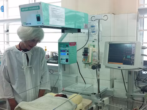 Bà Suzanna Lubran bên cạnh em bé sinh non nằm trên giường sưởi bà vận động tài trợ ngày 8/11