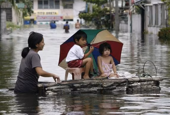 Một người mẹ dùng bè tự chế bằng xốp và tre nứa đưa con vượt lũ tại thị trấn Dampalit, thành phố Malabon, phía bắc Manila