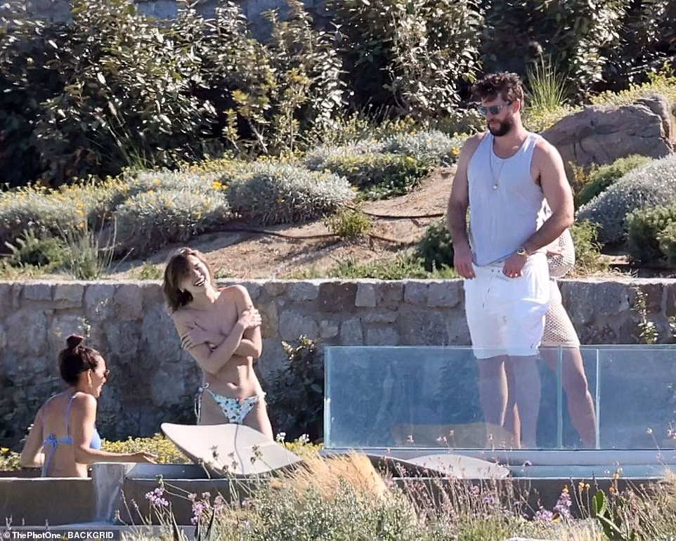 Chồng cũ Miley Cyrus đứng nhìn bạn gái (ở giữa) khoe vóc dáng gợi cảm trong trạng thái bán khỏa thân. Chân dài Australia bắt đầu được chú ý nhiều sau khi hẹn hò Liam. Cô từng hợp tác với các thương hiệu lớn như Chanel, đồ bơi Seafolly...