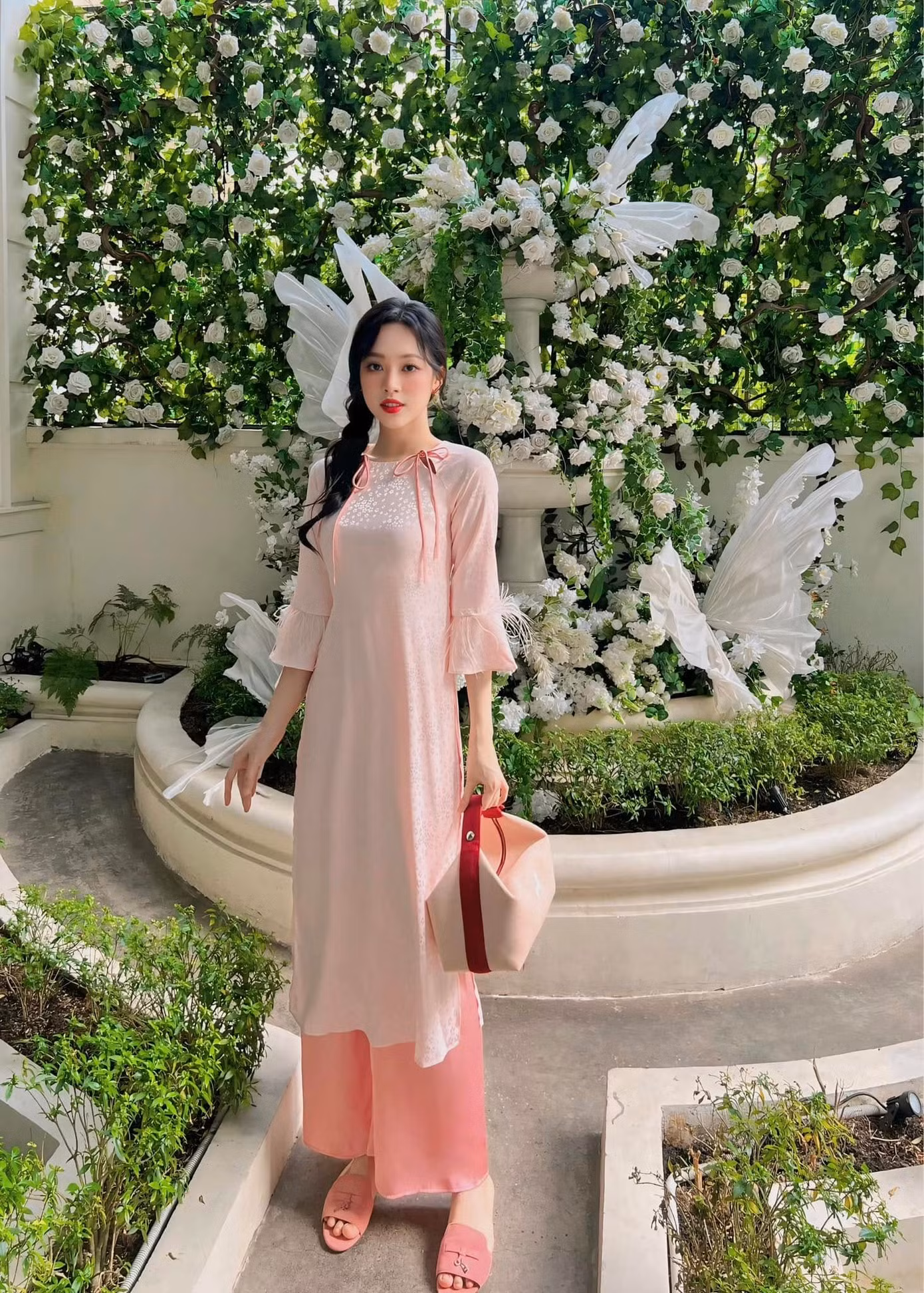 Á hậu Trịnh Thùy Linh chọn áo dài tông màu hồng pastel dịu dàng. Cô khéo léo phối cùng túi xách, dép bệt cùng tông màu. Người đẹp Thanh Hóa được khen khéo léo chọn áo dài tôn số đo ba vòng chuẩn.