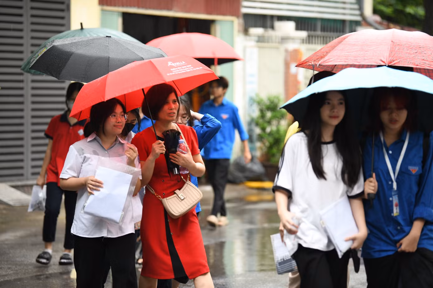 Thời tiết mưa gió các em học sinh được mẹ che ô cho vào cổng trường thi. Ảnh: Như Ý