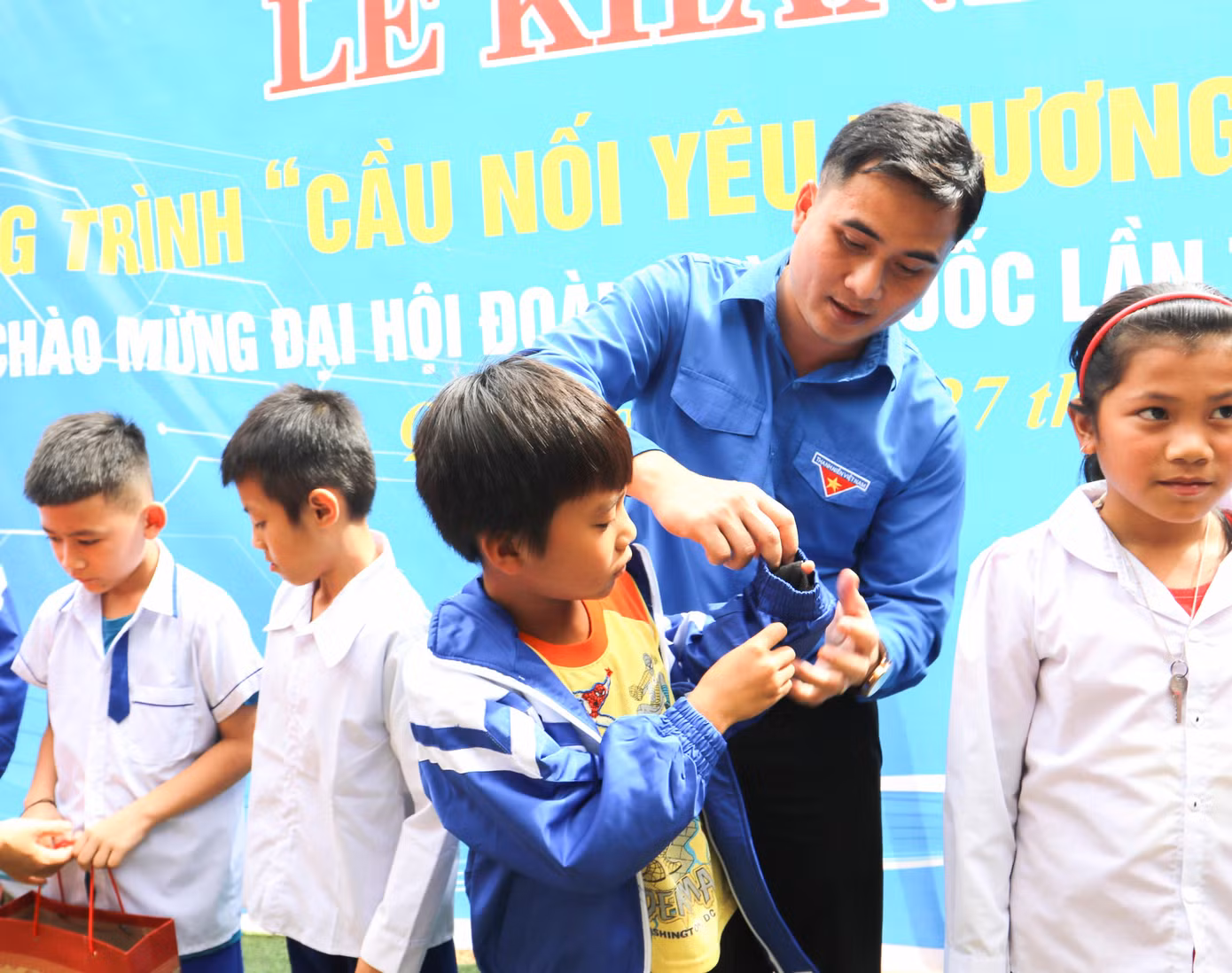 Từ chiếc cầu làm động lực, nối đôi bờ suối Nậm Hinh, bản Khủn Na sẽ khoác lên mình màu áo mới như chính chiếc áo mà các em nhỏ đang được mặc lên. Trong ảnh: Anh Thái Minh Sỹ - Phó Bí thư Thường trực Tỉnh Đoàn Nghệ An mặc áo mới cho em học sinh.