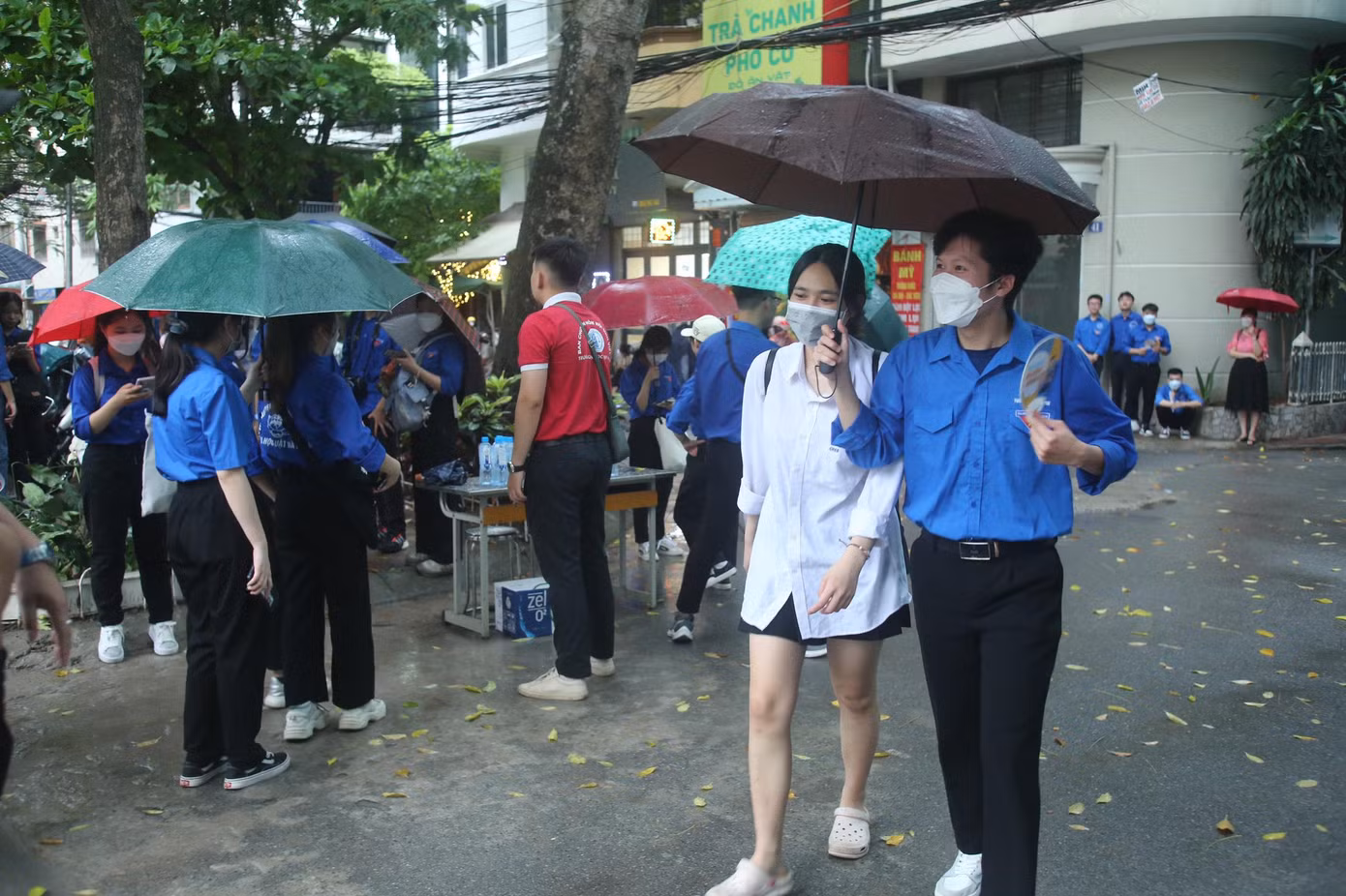 Áo xanh tình nguyện đội mưa che ô cho thí sinh từ cổng vào đến phòng thi trước giờ tập trung.