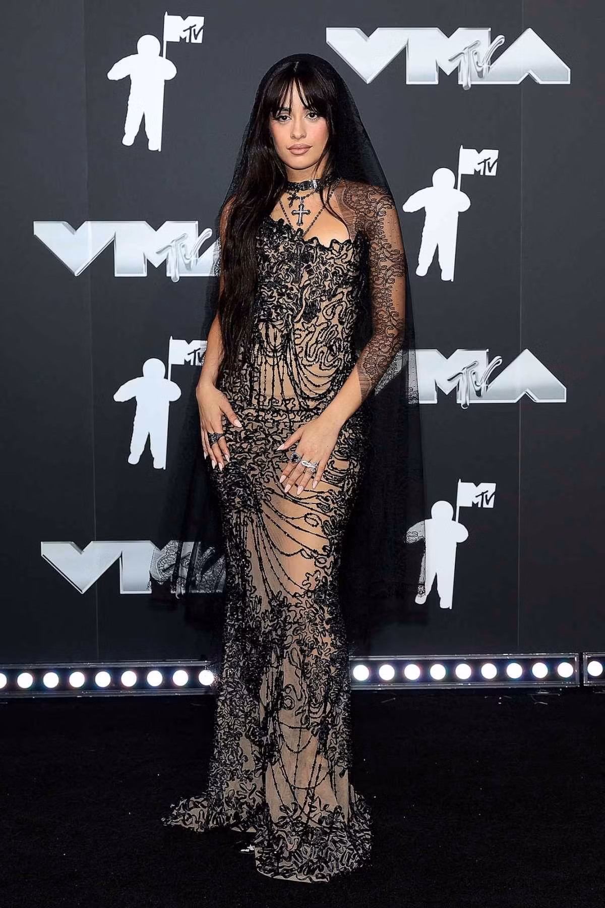Từ bỏ mái tóc vàng hoe từng giới thiệu trong đĩa đơn C, XOXO "I Luv It", Camila Cabello quay lại với tóc đen thương hiệu. Cựu ngôi sao của Fifth Harmony khoe vóc dáng trong chiếc váy đính hạt Tony Ward mỏng manh. Cô kết hợp vẻ ngoài này với mạng che mặt mỏng manh và vòng cổ thánh giá.