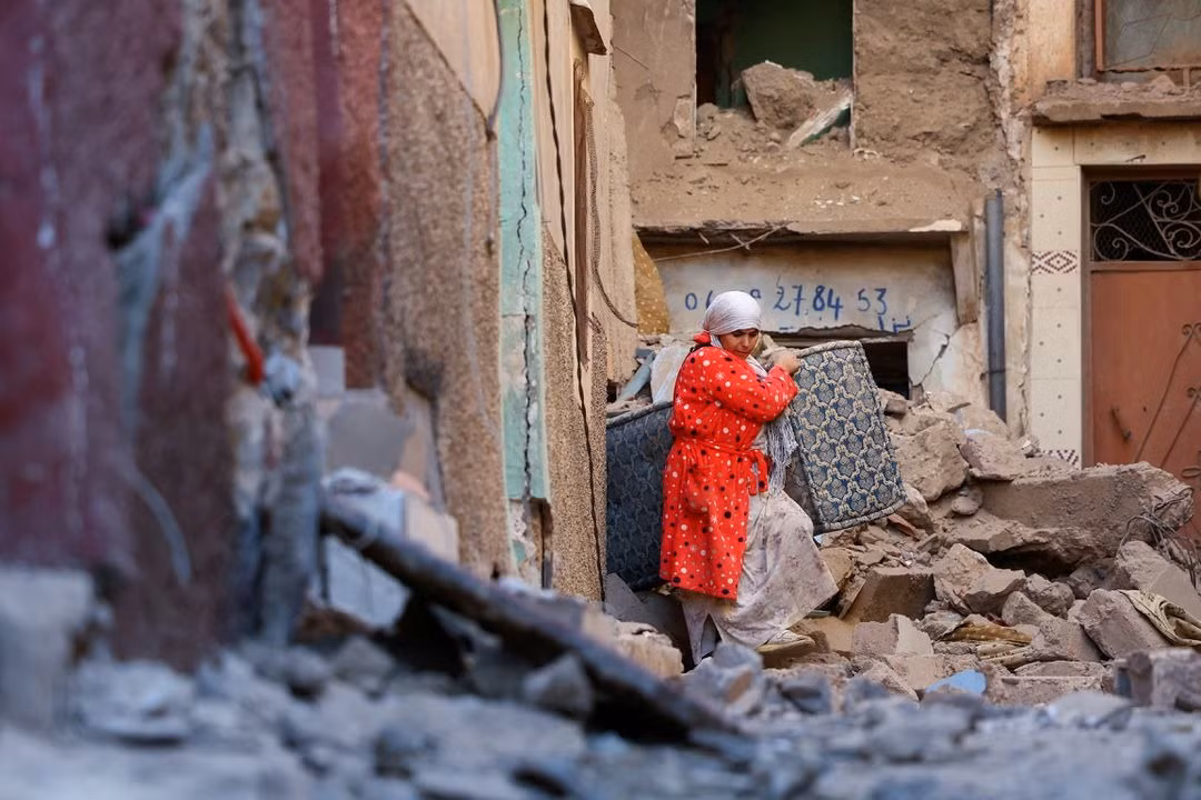 Một phụ nữ mang tài sản ra khỏi một ngôi nhà bị phá huỷ ở Moulay Brahim. Ảnh: Reuters