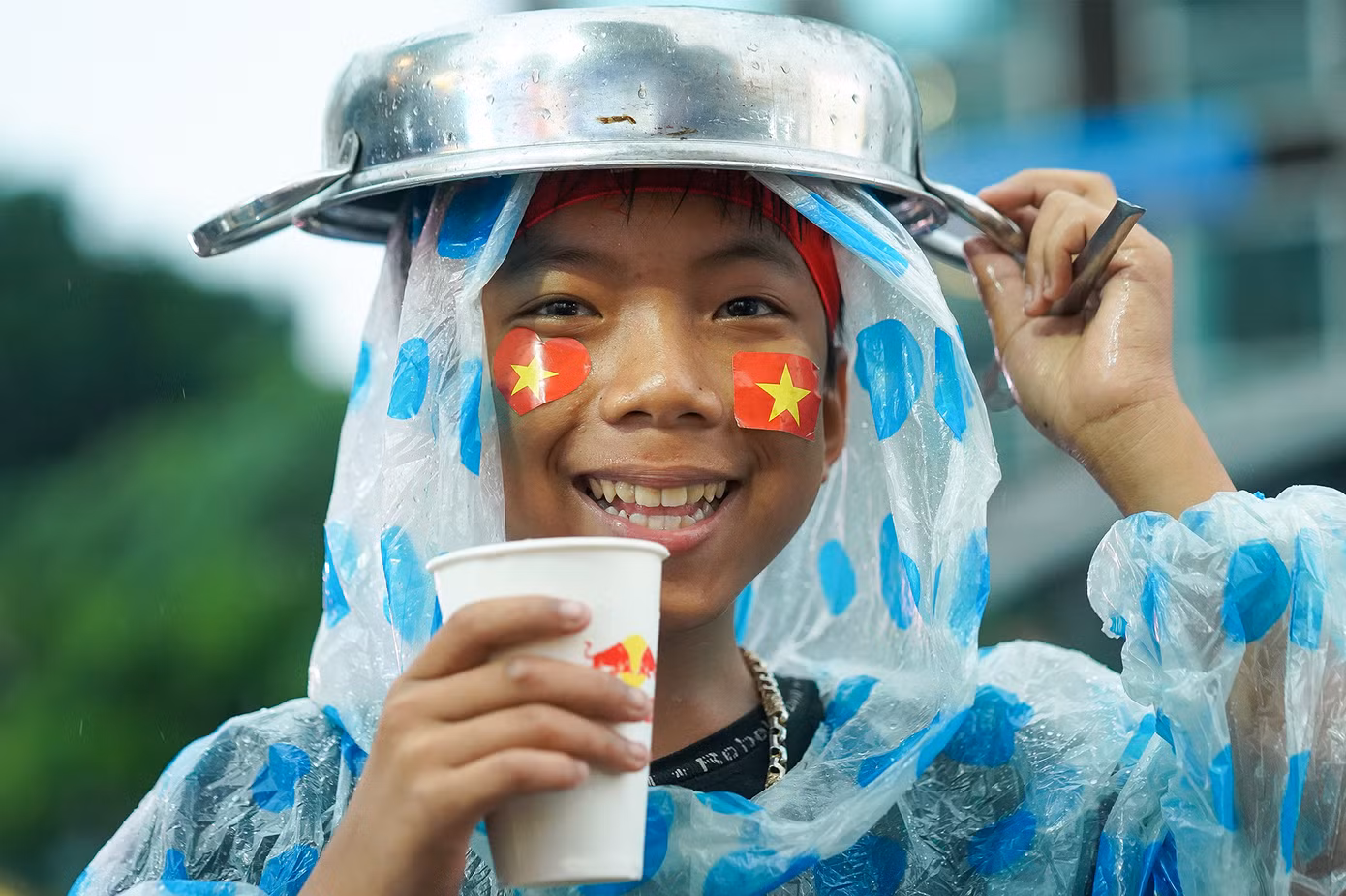 Một em nhỏ tận dụng chiếc nồi tạo âm thanh cổ vũ để che mưa.