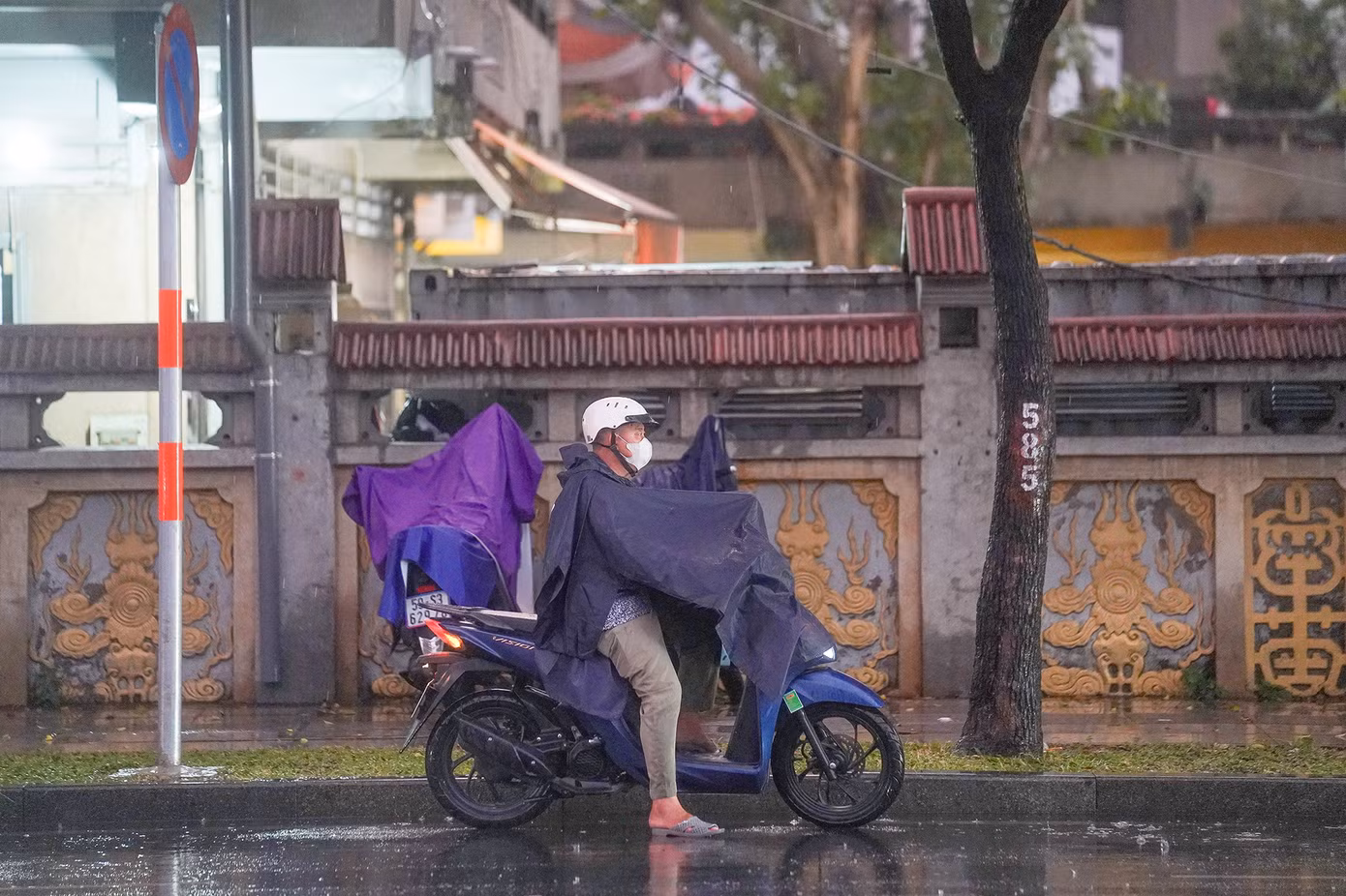 Một người đàn ông vừa dừng xe lại mặc áo mưa nhưng chưa đi vội vì tầm nhìn đang bị hạn chế khi ông vừa ra từ bãi xe chùa Vĩnh Nghiêm.