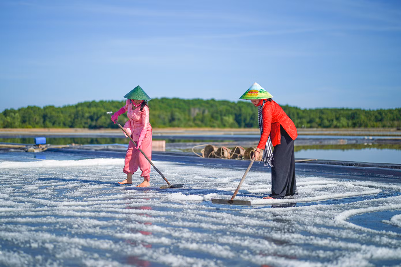 Hiện tại Thiềng Liềng có khoảng 10 hộ dân làm dịch vụ du lịch cộng đồng, mỗi hộ chuyên một sản phẩm như ngâm chân thư giãn tại nhà cô Năm Tuyết, ăn trưa nhà cô Năm Đổi, Sâm sâm giải nhiệt hộ Sáu Trúng; nước mát và lưu trú hộ Mười Giạ... Ảnh: Chị Nguyễn Thị Bạch Tuyết (áo đỏ) - Giám đốc HTX Nông nghiệp TM DV DL Thiềng Liềng đang giới thiệu với du khách quy trình thu hoạch muối của diêm dân.