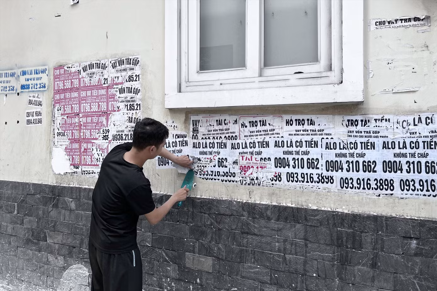 Công an đưa một bị can đi cạo xóa các tờ rơi quảng cáo vay tiền dán trên tường