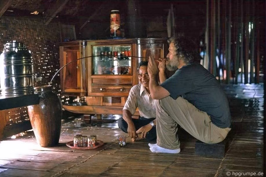 Hans-Peter Grumpe uống rượu cần bằng ống hút dài trong buổi đón tiếp của gia đình ông Mamahrine tại làng Ê Đê Ko Dhong, gần Buôn Ma Thuột, năm 1992.
