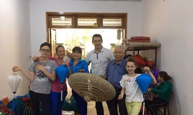 Cụ Huỳnh Văn Ba chụp hình lưu niệm với du khách tại xưởng đèn lồng của gia đình
