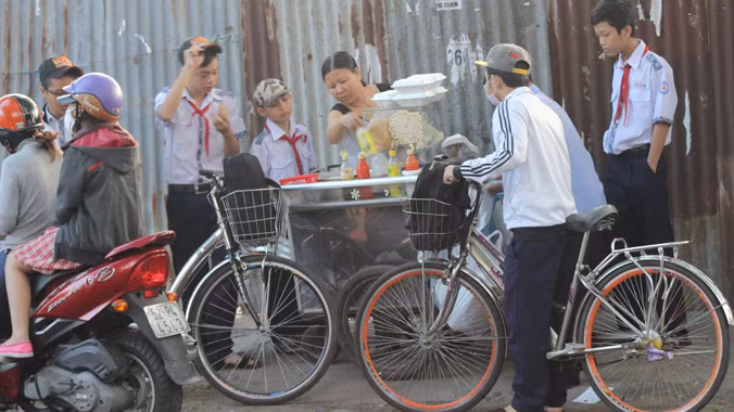 Học sinh Trường THCS Hoàng Hoa Thám phải mua bánh mì, xôi… ngay tại cổng trường ăn cho kịp giờ học buổi sáng. Ảnh: Ngô Đào